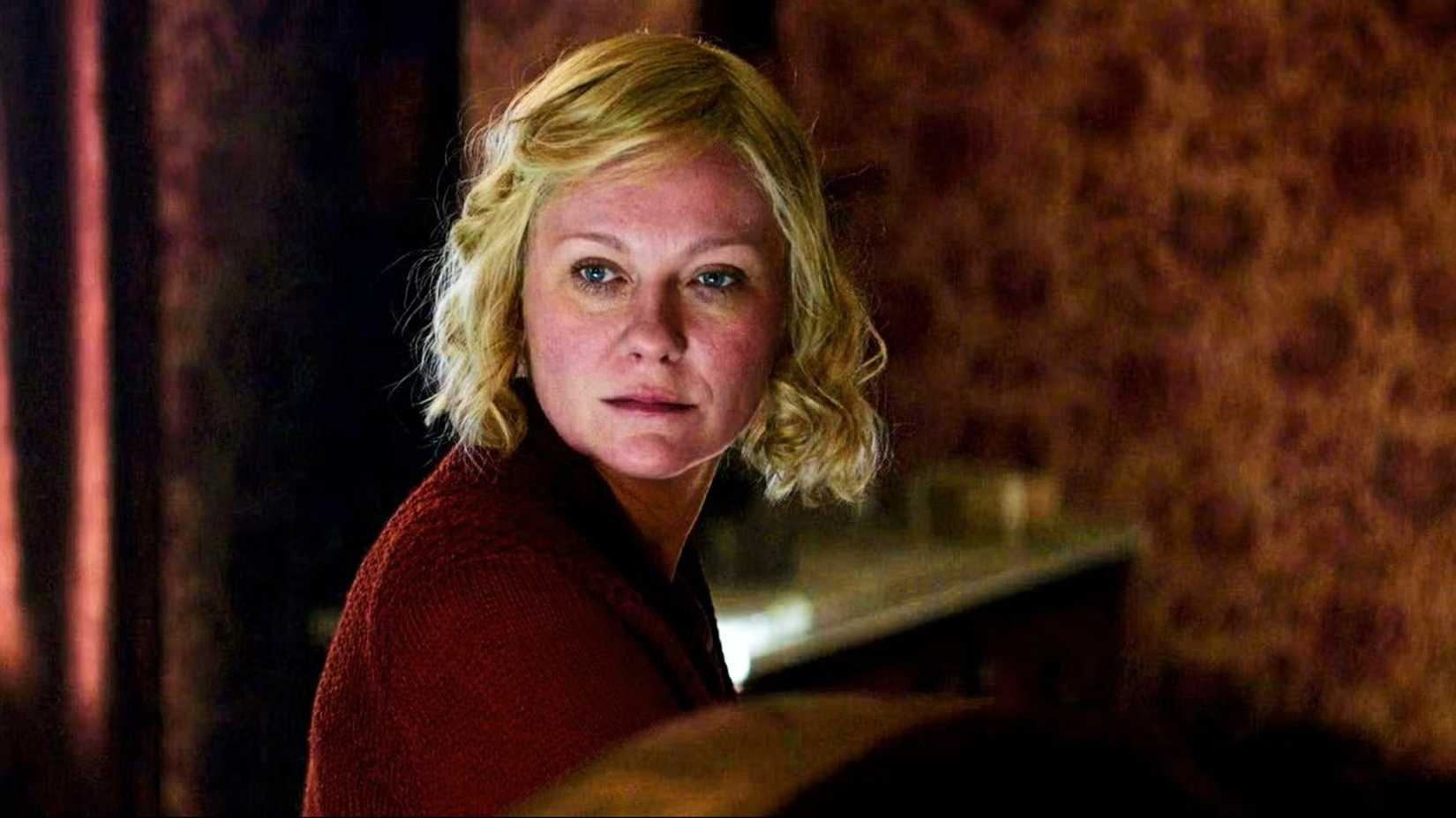 Kirsten Dunst als Rose Gordon sitzt in „The Power of the Dog“ im roten Raum und trägt einen Pullover