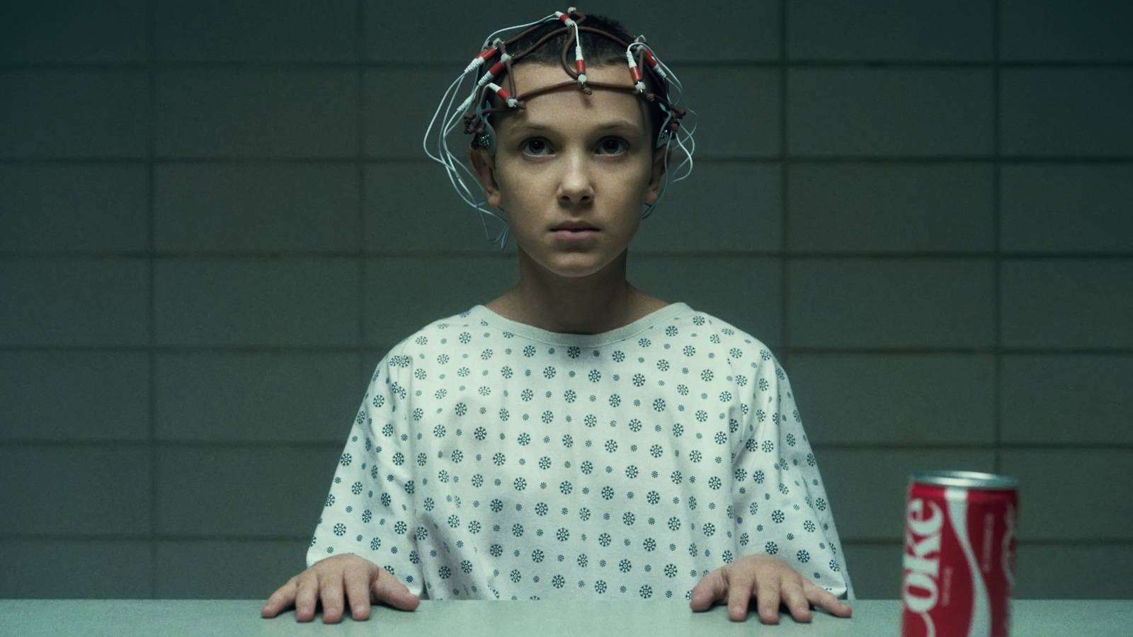 Eleven (Millie Bobby Brown) with scientific equipment attached to her head as she's observed at Hawkins Lab in Stranger Things season 1