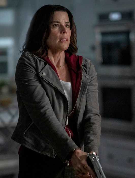 Neve Campbell looks nervous while holding a gun inside a dark house in a scene from Scream 7