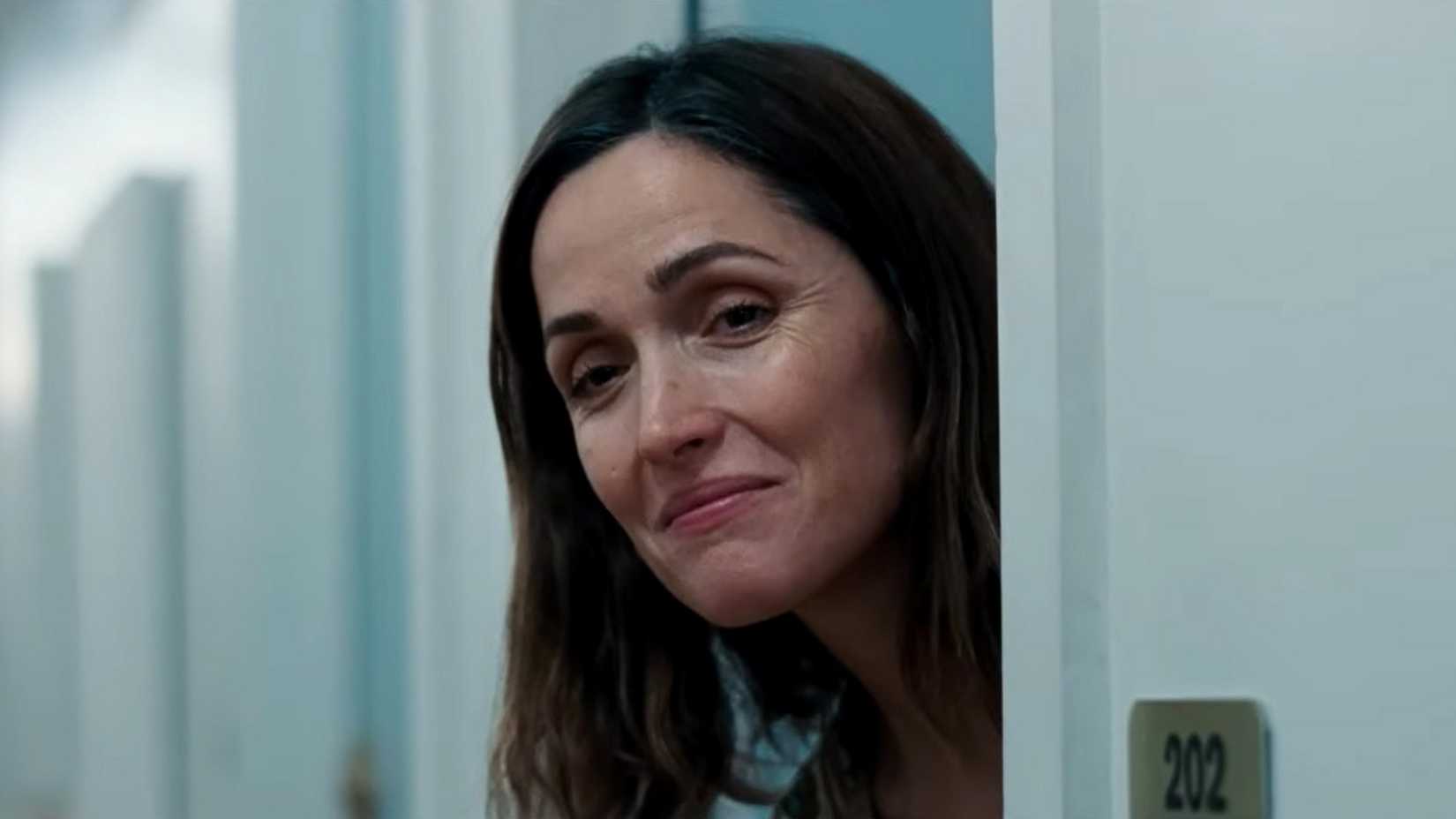 Rose Byrne peeking through a doorway with a smug expression in If I Had Legs I'd Kick You