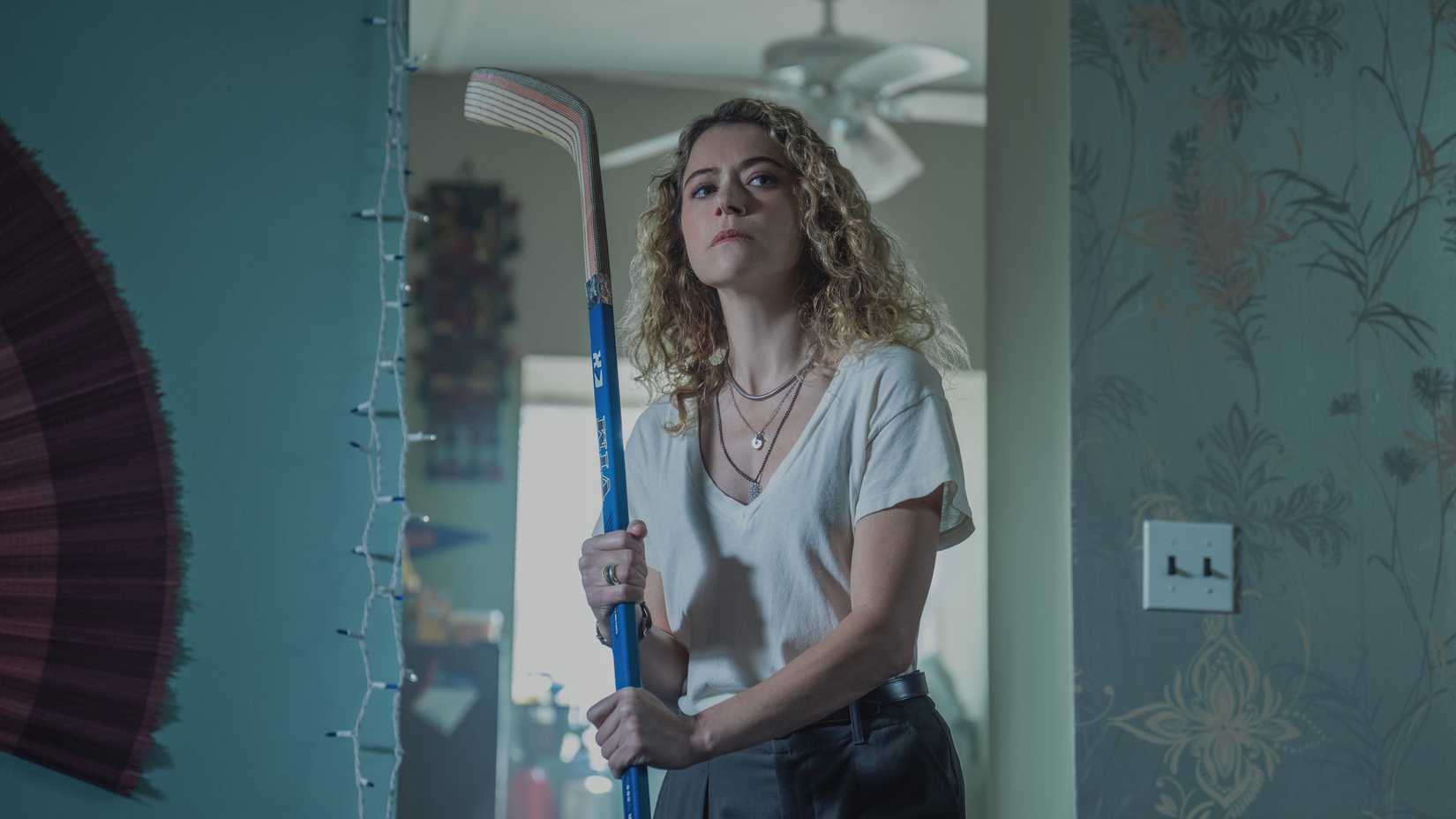 Tatiana Maslany als Paula, die einen Hockeyschläger in der Hand hält und vorsichtig dreinschaut, in „Maximum Pleasure Guaranteed“.