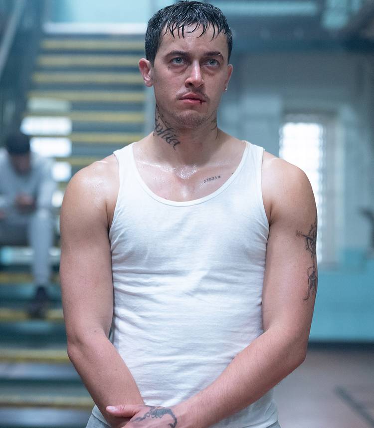 tom blyth s dee standing with his hands crossed and with a bloody lip in wasteman