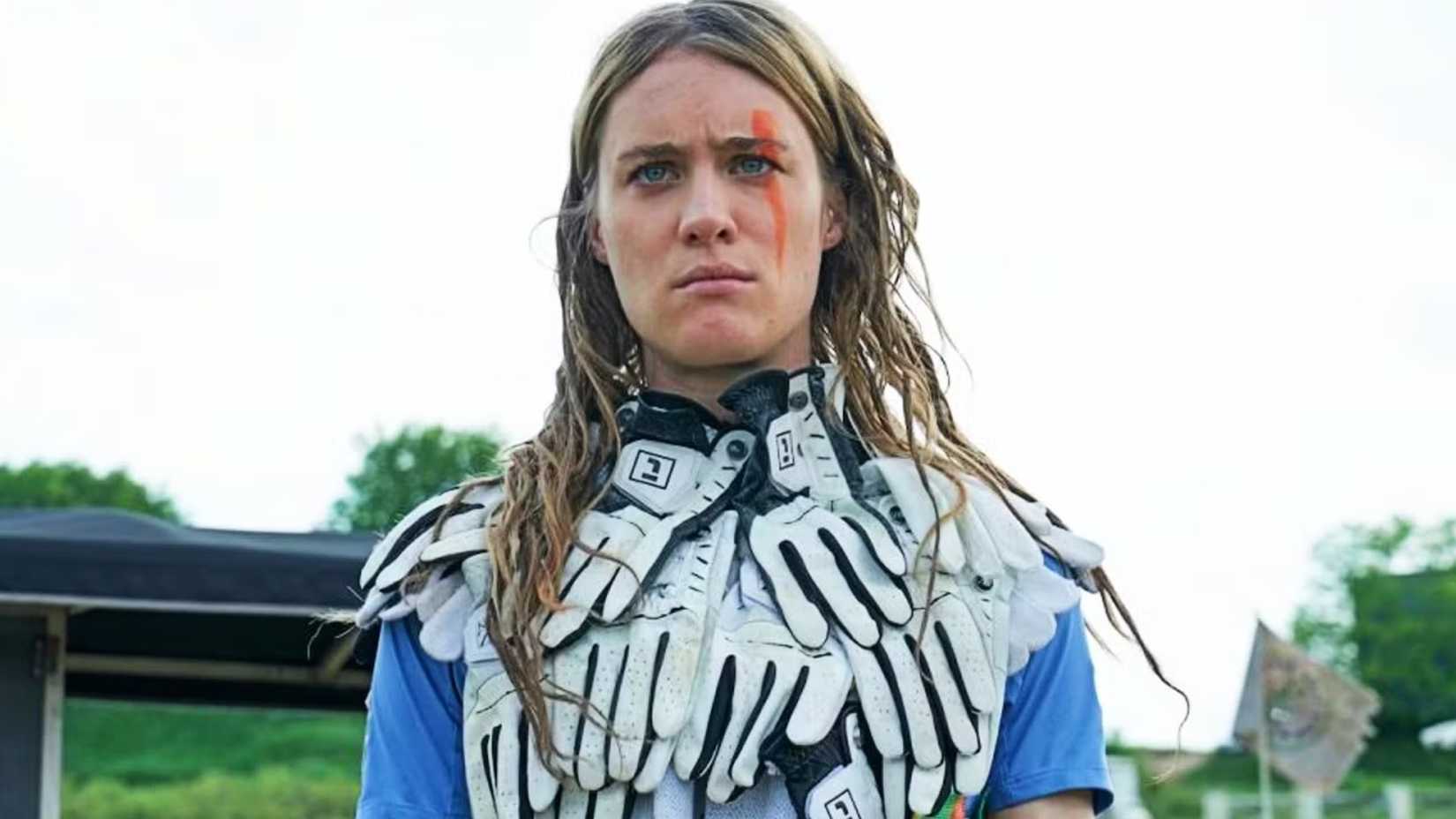 Mackenzie Davis como Kirsten em Station Eleven olha severamente com um colete feito de luvas