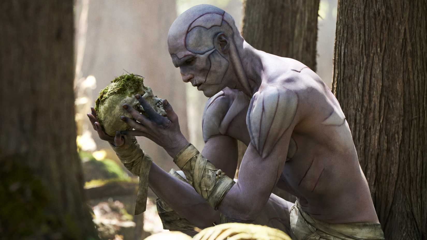 Jacob Elordi’s The Creature looking at a human skull in 2025’s Frankenstein