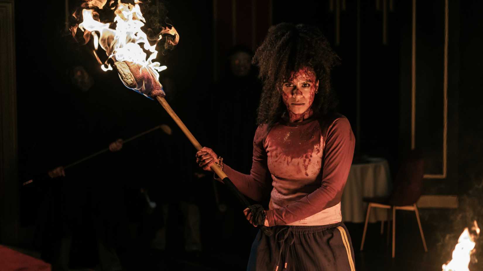 A bloodied Asia holding a flaming ax in They Will Kill You