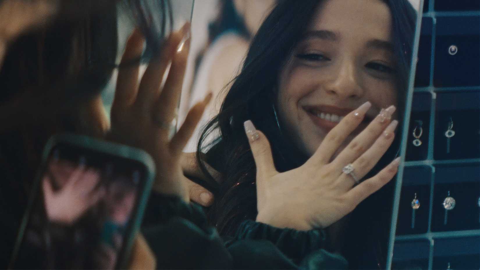 Anora sorrindo e mostrando seu anel no espelho em Anora