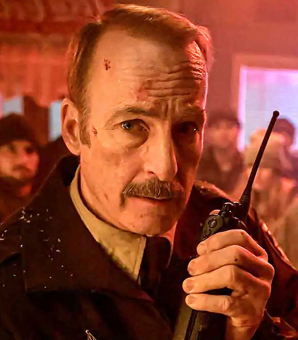 Bob Odenkirk's Sheriff Ulysses holding a walkie talkie looking worried in Normal Vertical-1