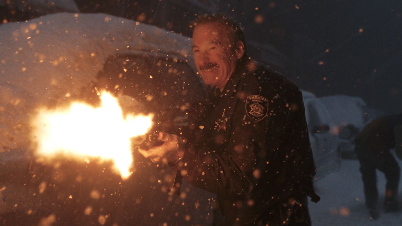 Bob Odenkirk's Ulysses firing an assault rifle next to a car in the snow in Normal