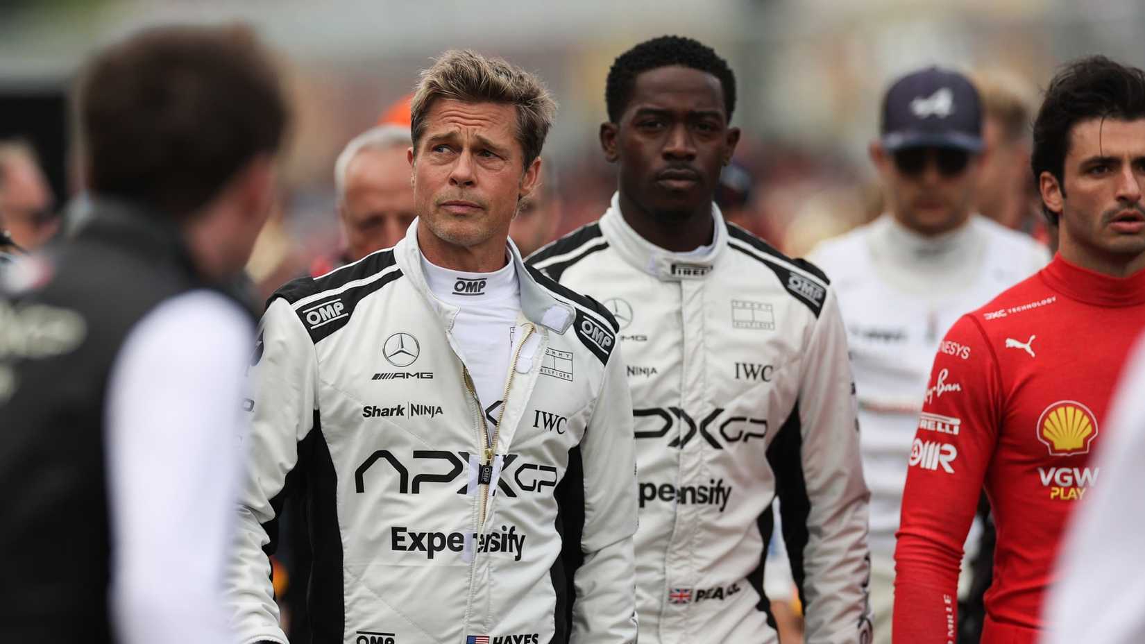 brad pitt and damson idris walk next to each other in their racing outfits in f1