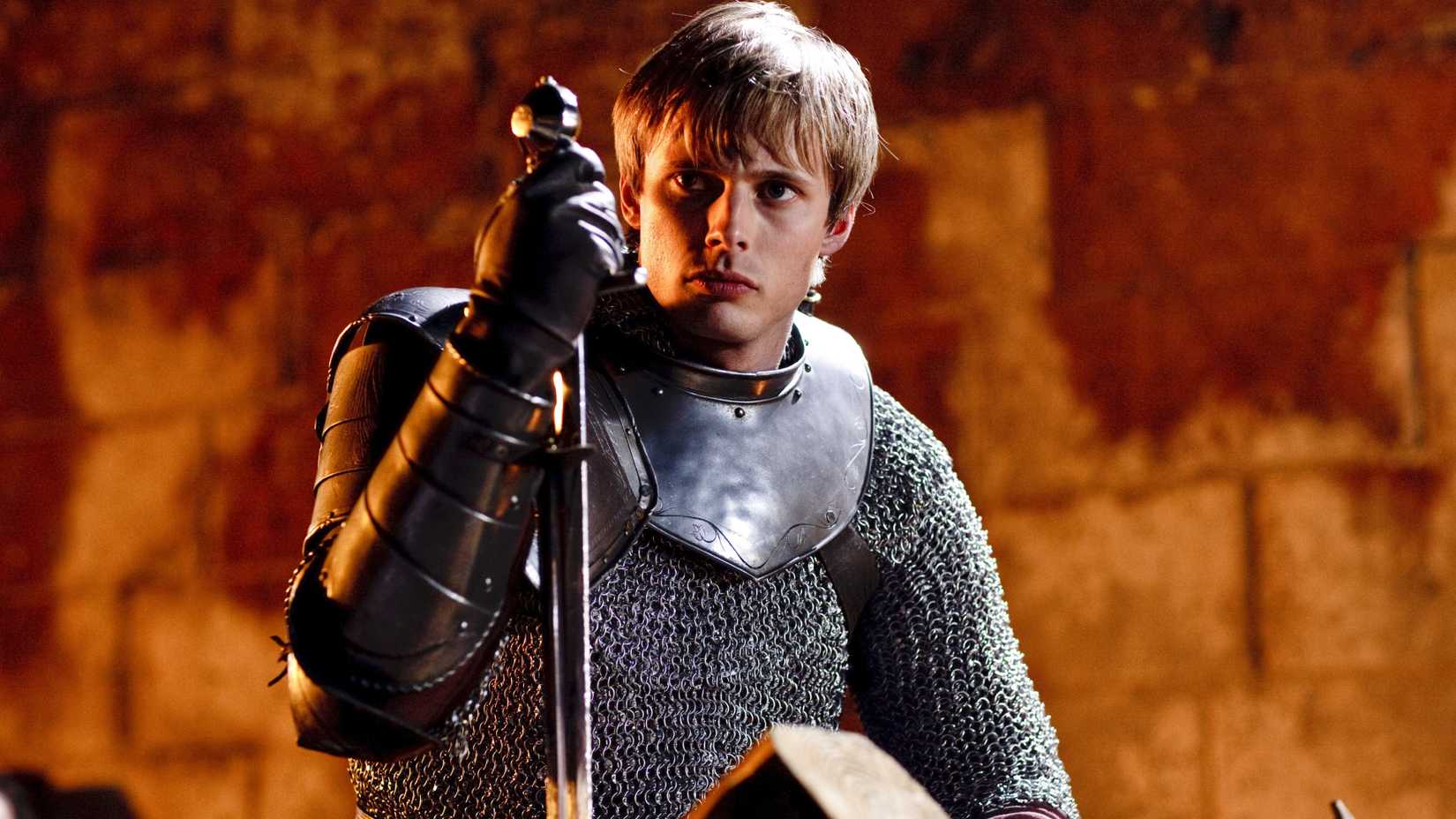 Bradley James as Arthur Pendragon leaning on his sword in Merlin