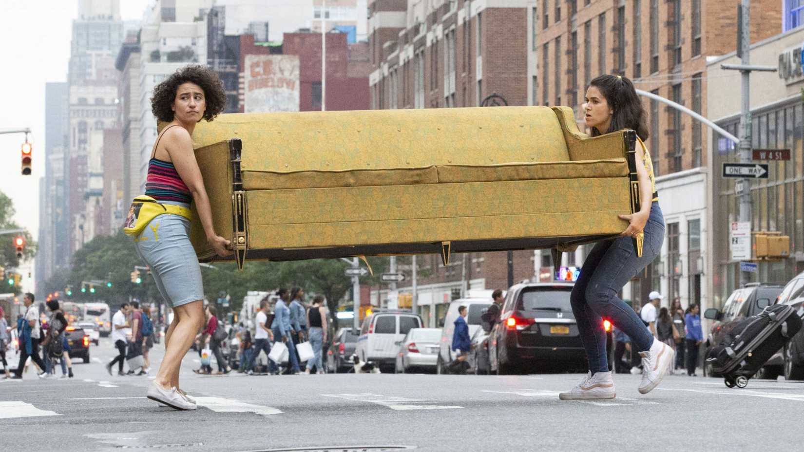 Ilana (Ilana Glazer) and Abbi (Abbi Jacobson) carrying a couch through a street in NYC in Broad City.