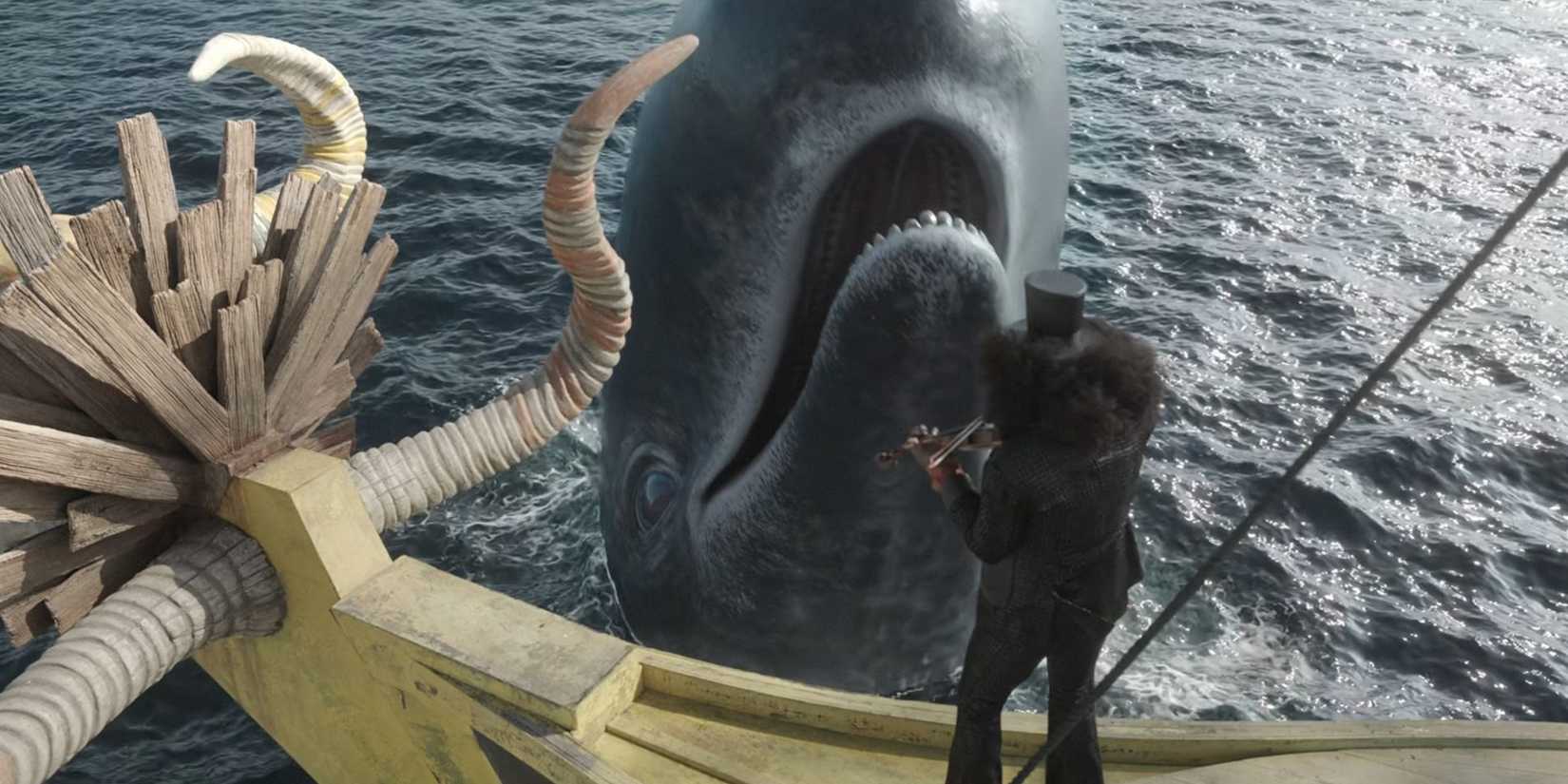 Imagem da 2ª temporada de One Piece Live Action da Netflix mostra Brook com seu afro e cartola tocando violino em seu barco com a baleia Laboon sorrindo à sua frente.