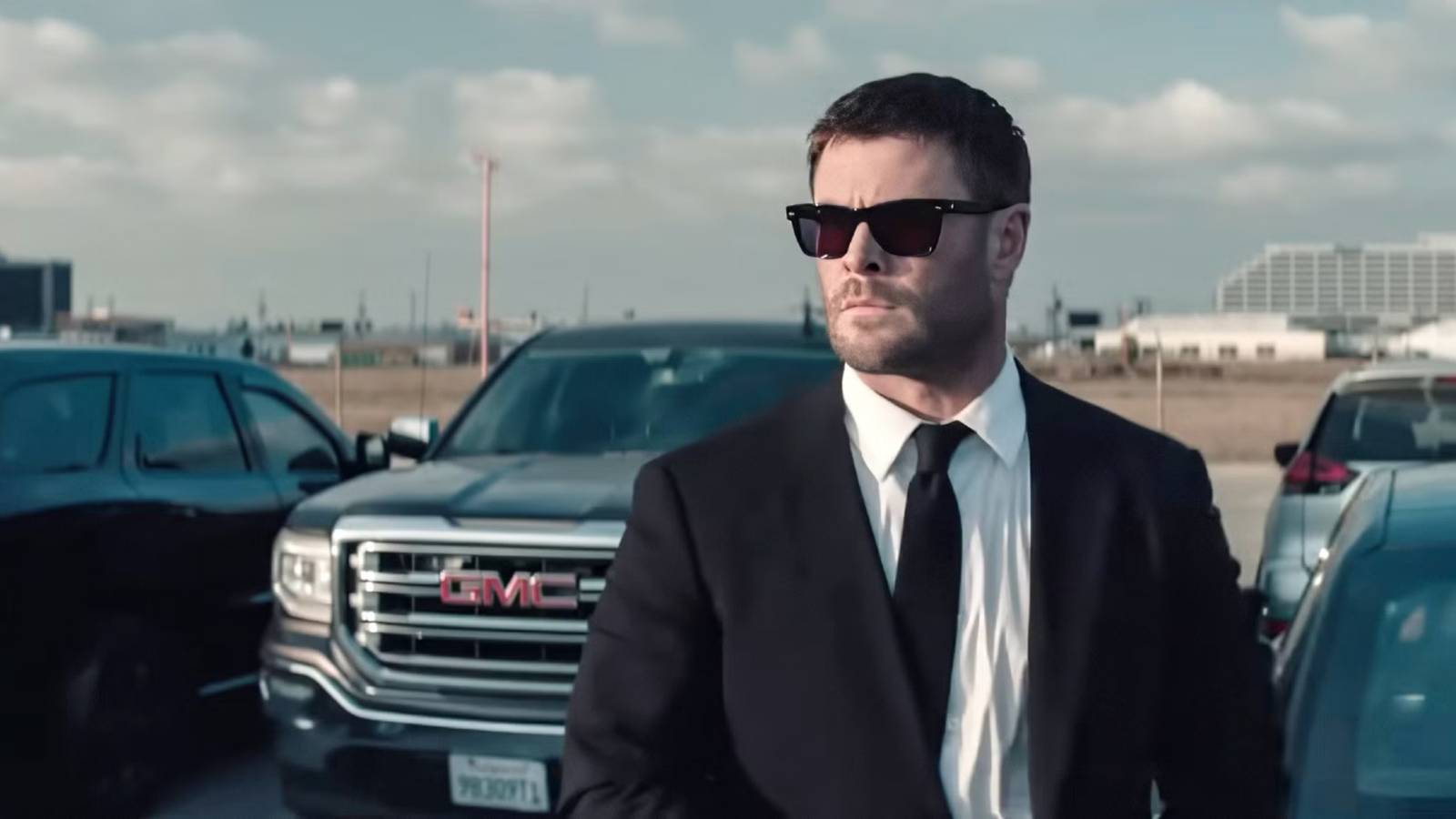 Chris Hemsworth with sunglasses on in front of a row of cars in Crime 101