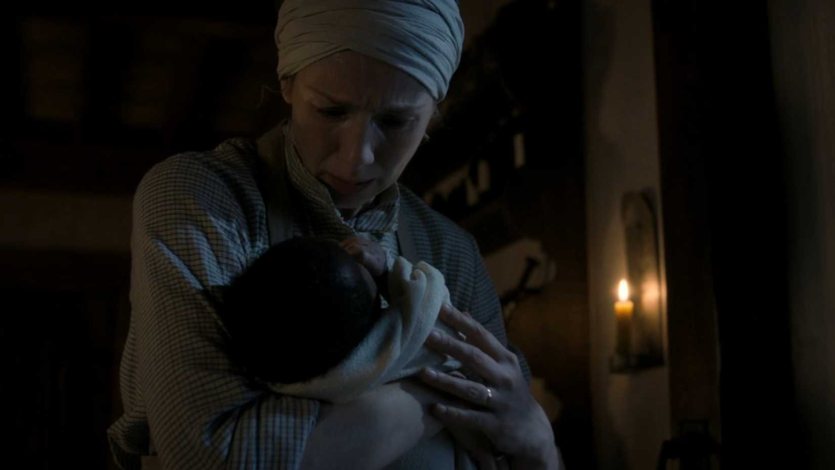 Claire looking amazed while holding a baby in Outlander season 8