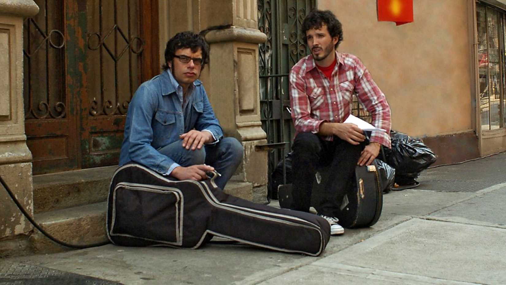 Brett e Jemaine sentados na rua com seus violões em Flight of the Conchords