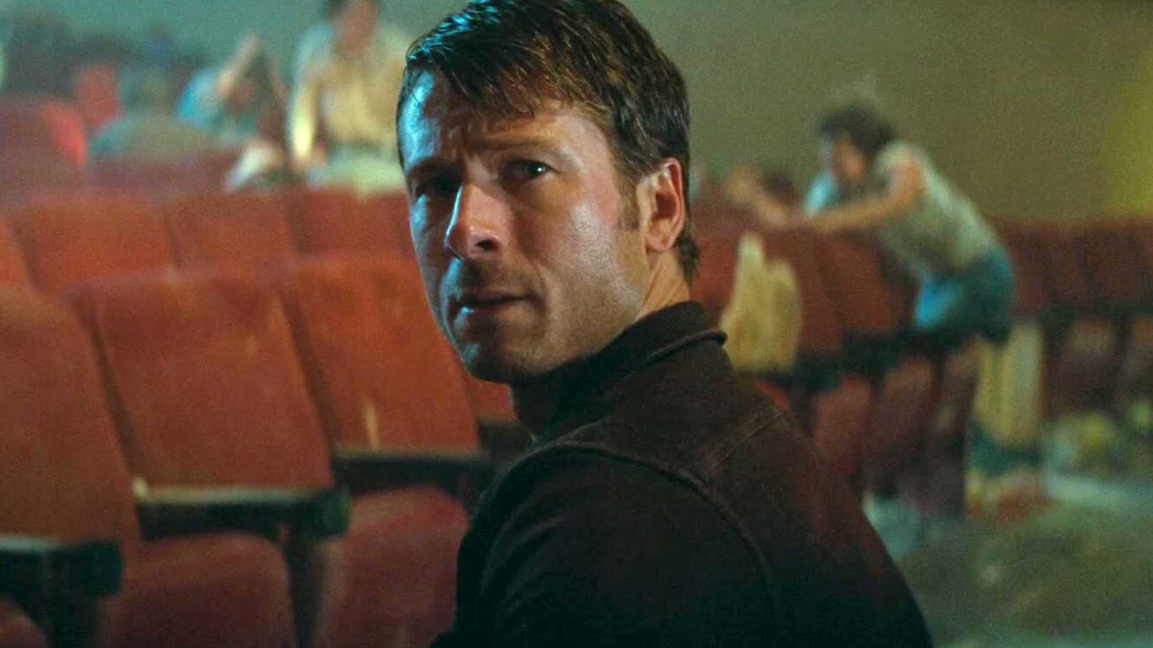 Glen Powell looking back over his shoulder in a theater in Twisters