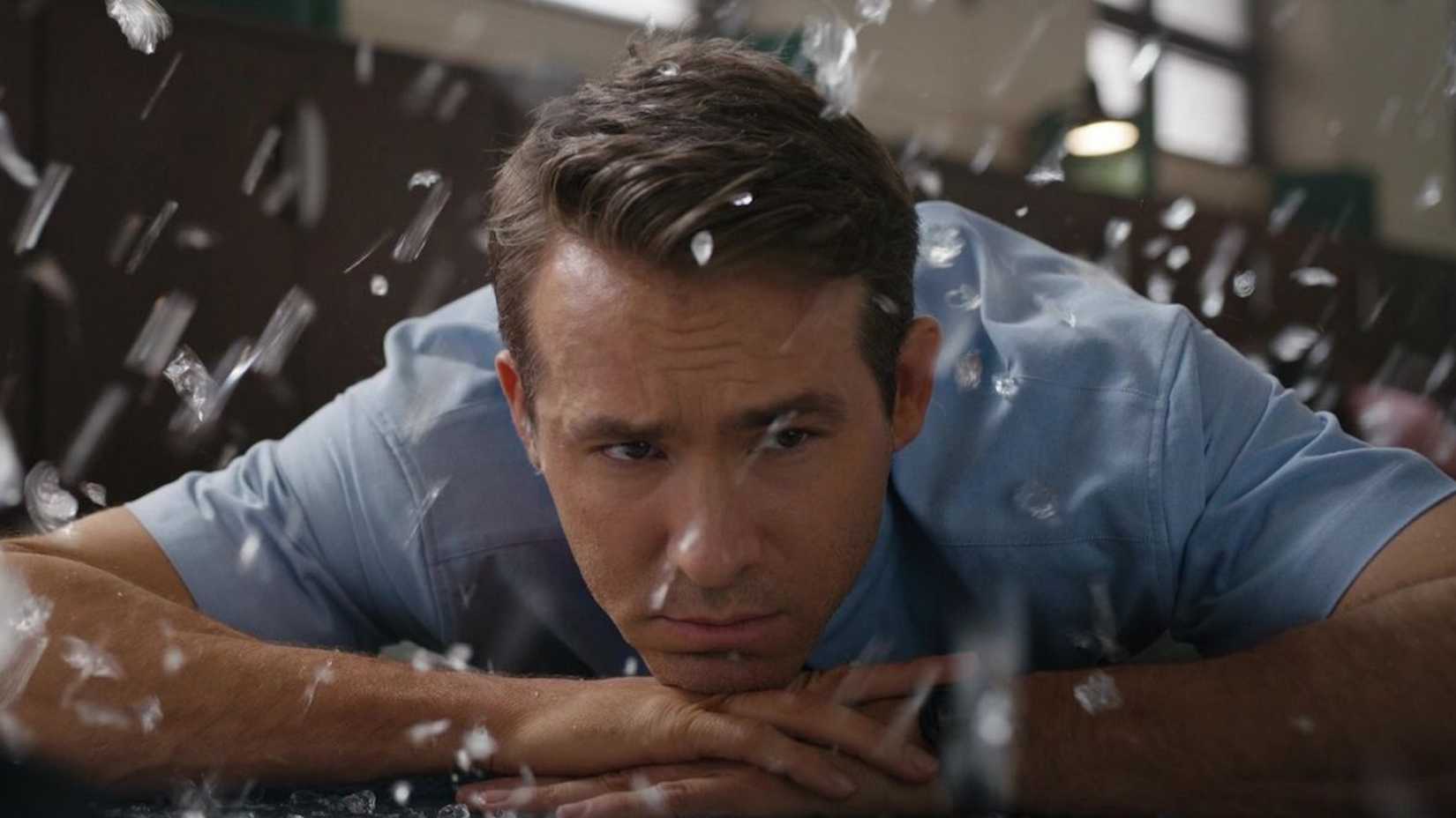 Guy (Ryan Reynolds) deitado calmamente no chão, coberto de cacos de vidro em Free Guy