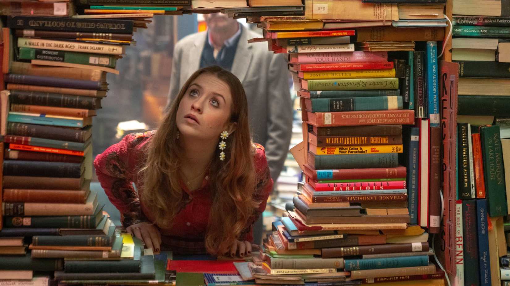 Mairead Tyers looking through a hole in a stack of books in Extraordinary