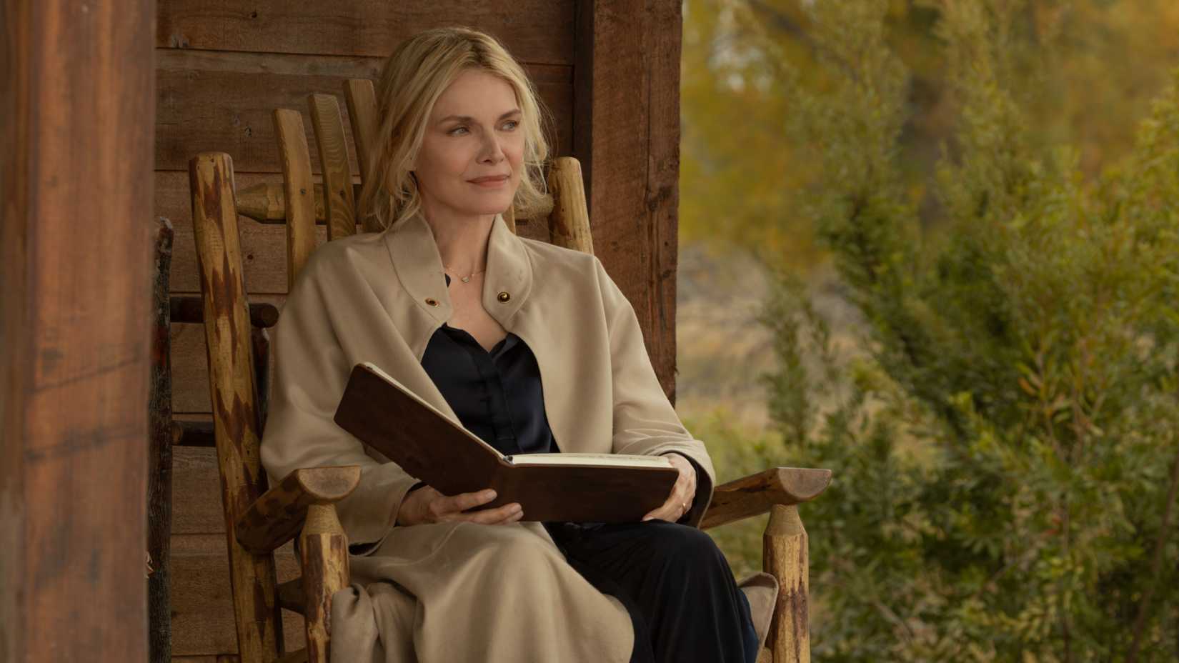 michelle pfeiffer s stacy holding a book and sitting on the porch while smiling in the madison 1
