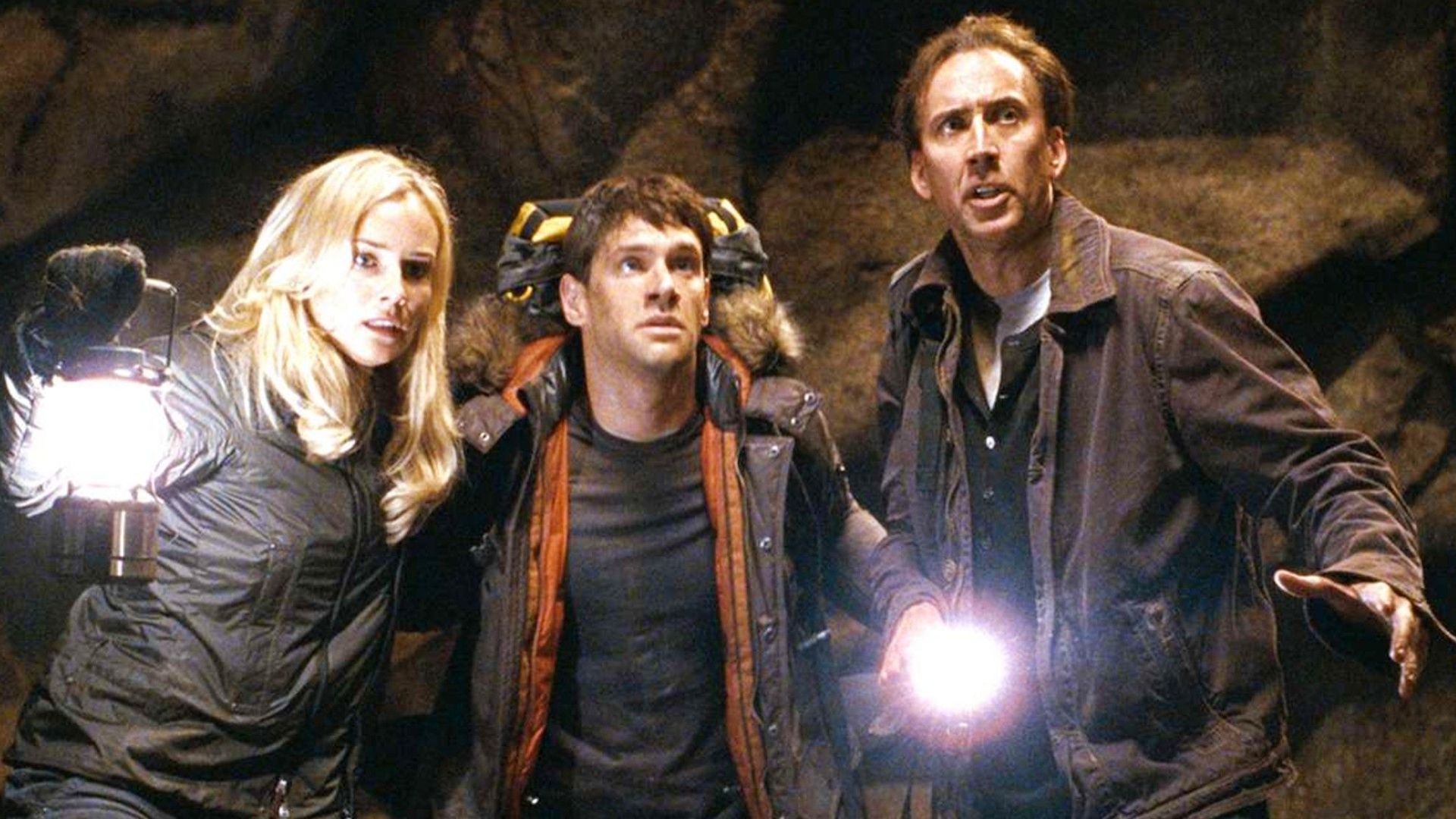 Nicolas Cage, Diane Kruger e Justin Bartha explorando uma caverna em A Lenda do Tesouro Perdido