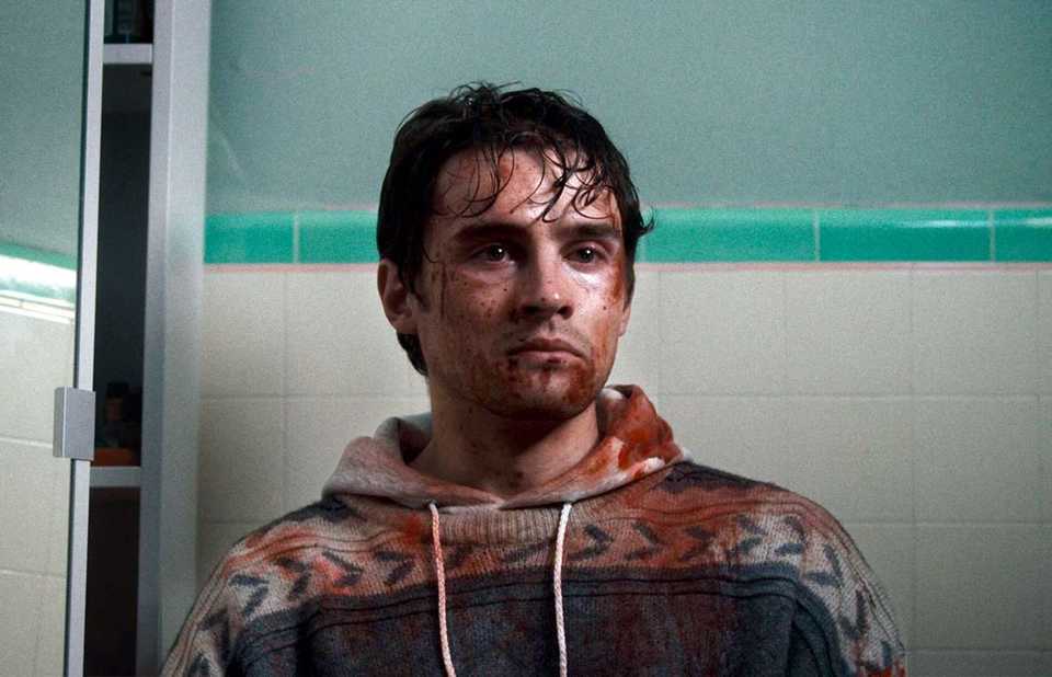 Michael Johnston stands in a bathroom and stares off into space while covered in blood and Obsession