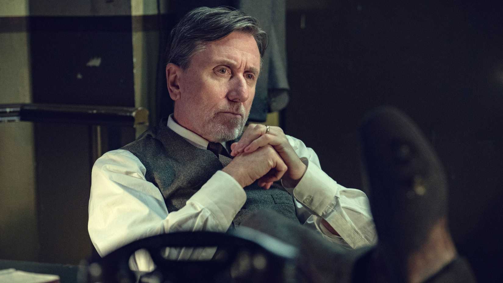 Peaky Blinders: The Immortal Man Ending Explained 1 Tim Roth as John Beckett sitting down with his hands pressed together in Peaky Blinders: The Immortal Man