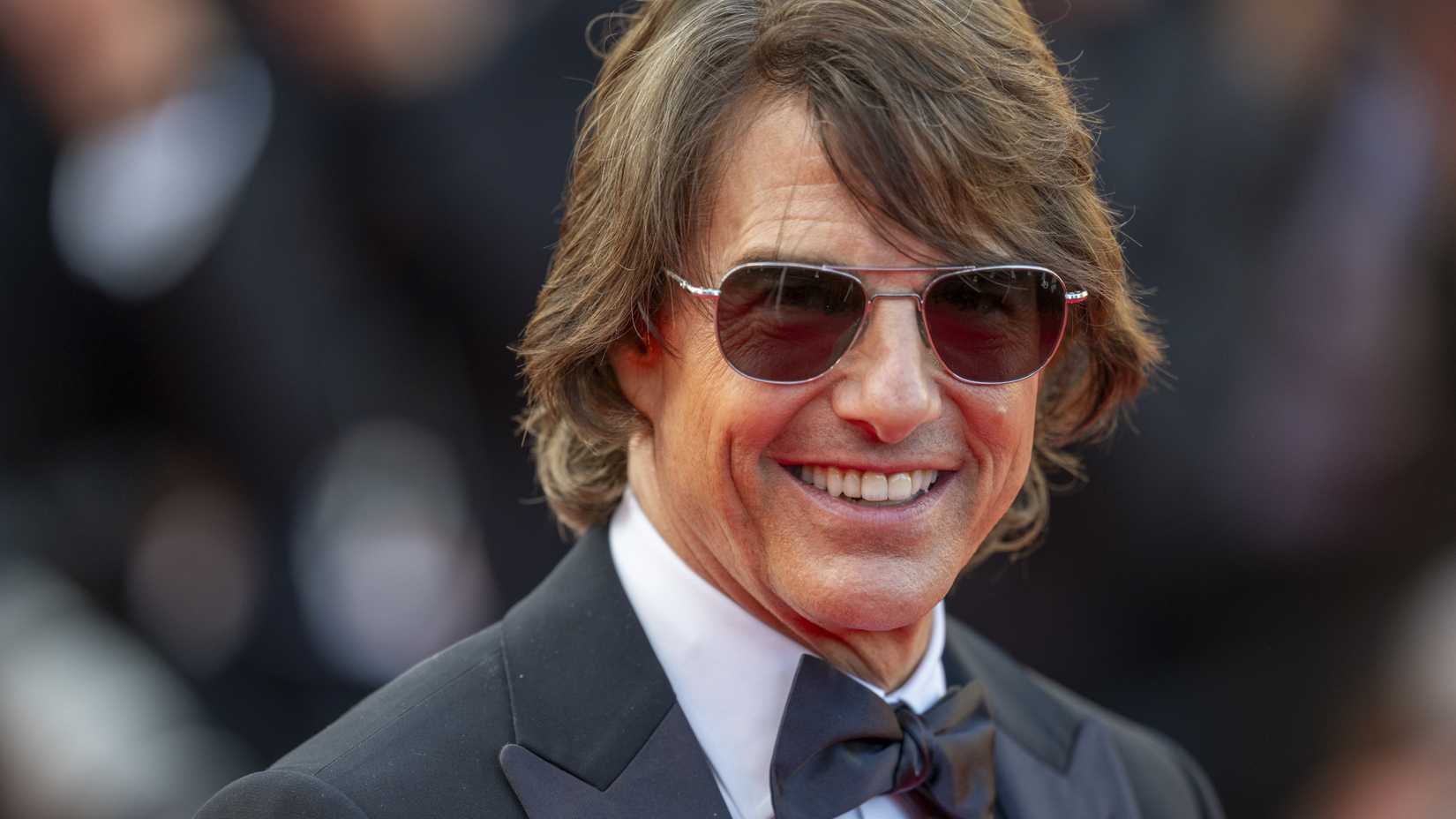 Tom Cruise sorri em um tapete vermelho