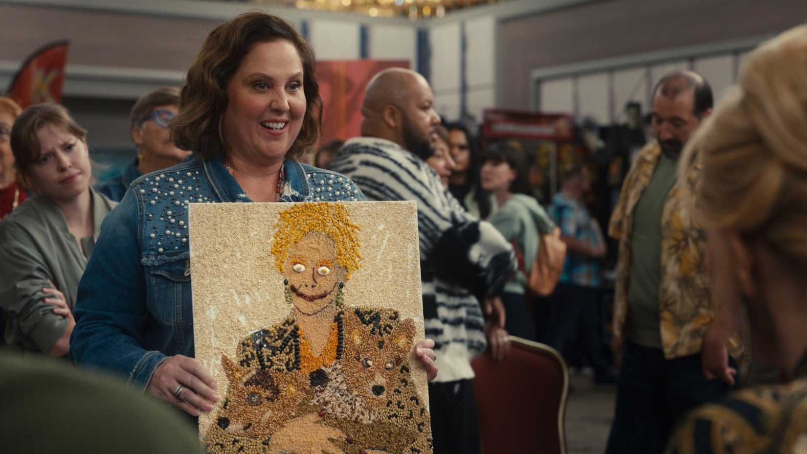 Bayne Gibby segurando um retrato caseiro de Deborah Vance em Hacks, temporada 5, episódio 2