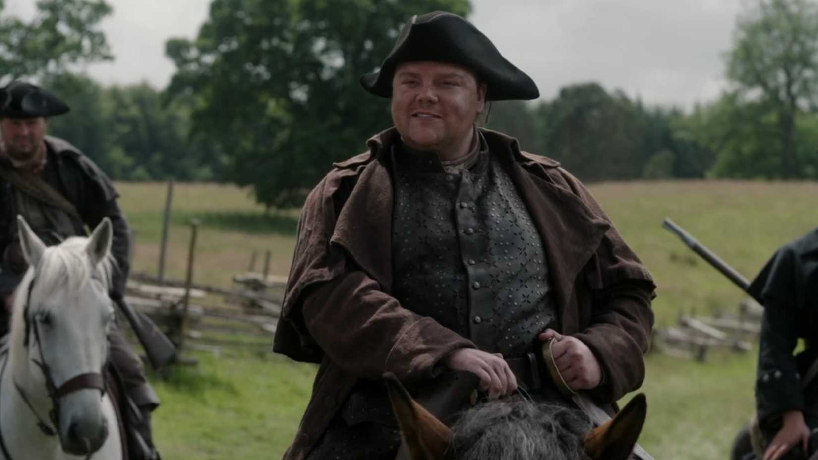 Jamie Makes A Deal With The Devil 3 Benjamin Cleveland smiling while sitting on his horse in Outlander season 8