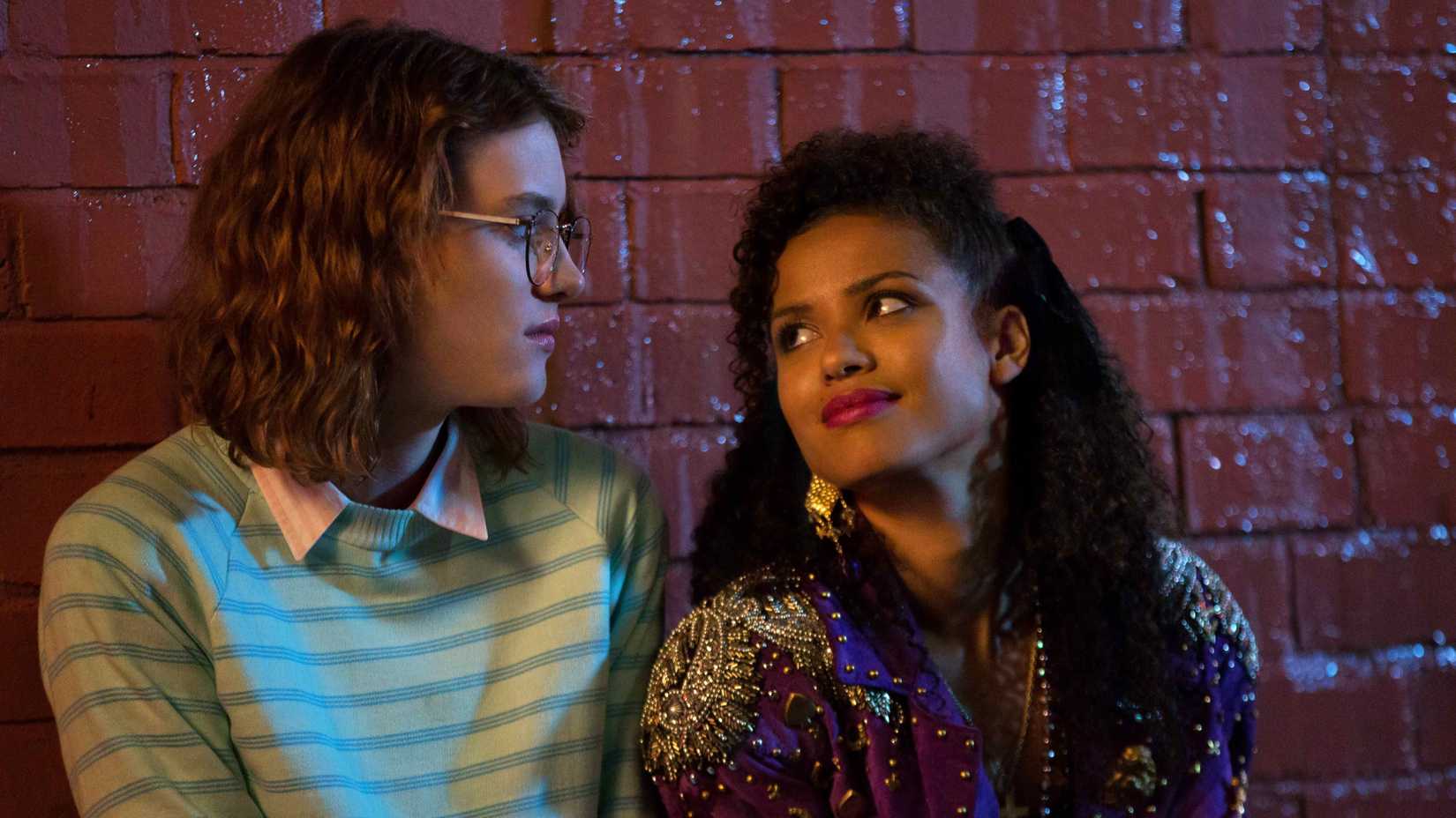 Yorkie (Mackenzie Davis) and Kelly (Gugu Mbatha-Raw) smiling at one another in Black Mirror, San Junipero.