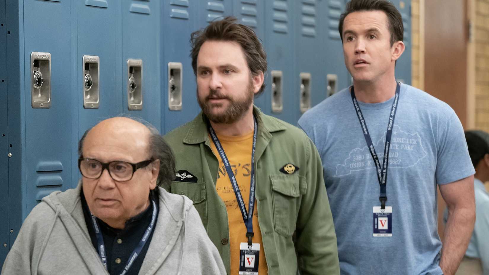 Danny DeVito, Charlie Day, and Rob Mac standing in front of school lockers and wearing lanyards in the It's Always Sunny Abbott Elementary crossover