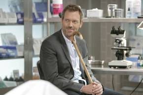 Hugh Laurie as Gregory House smiling while sitting down and holding his cane in House