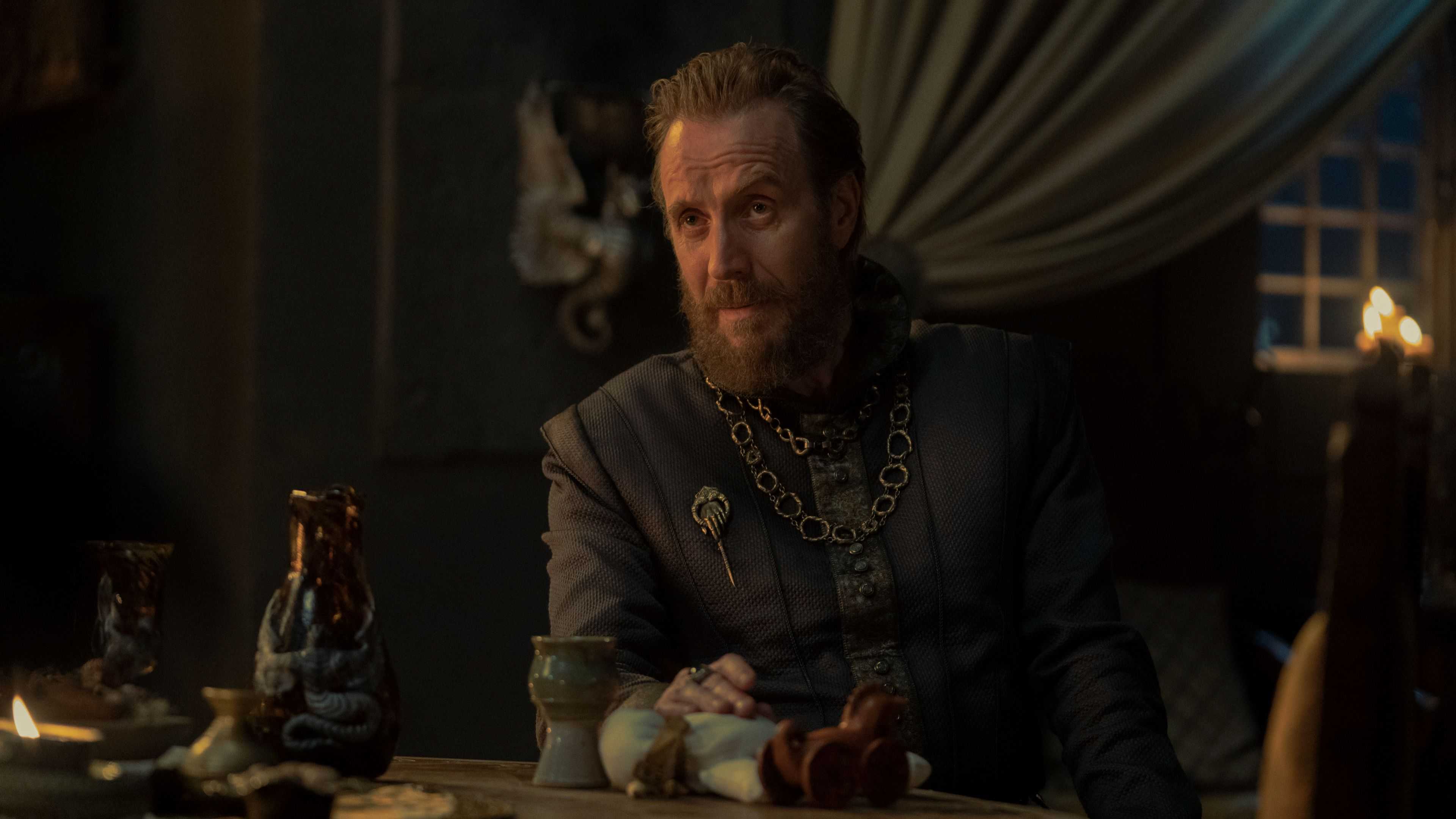 Otto Hightower (Rhys Ifans) looking at someone over a dinner table in House of the Dragon.