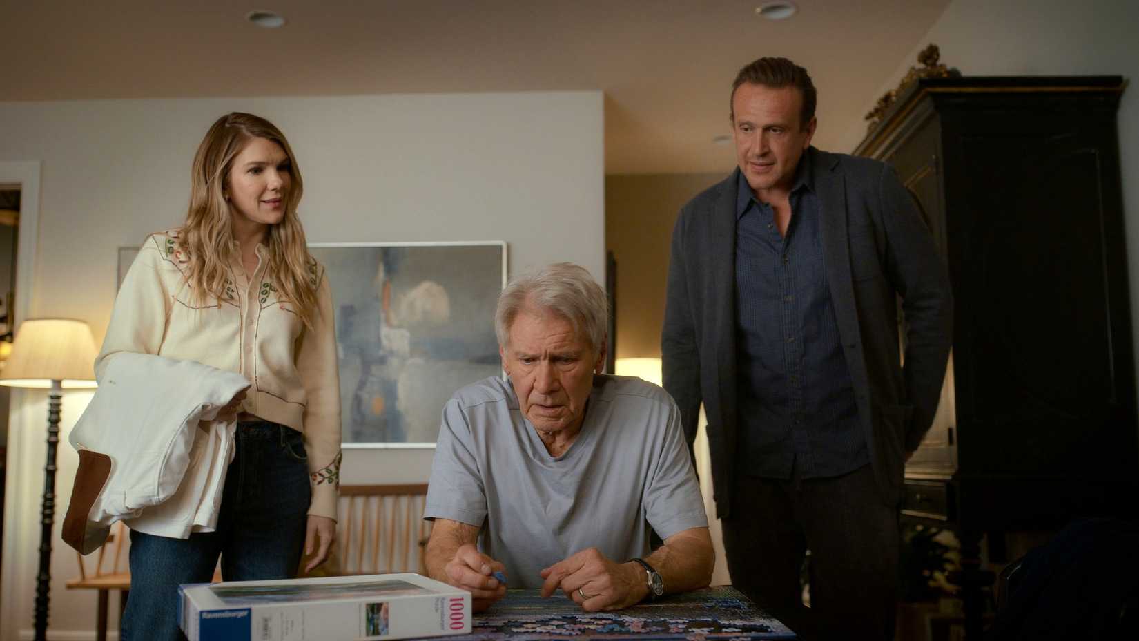 Lily Rabe as Meg and Jason Segel as Jimmy looking down at Harrison Ford as Paul as he works on a puzzle in Shrinking season 3, episode 5