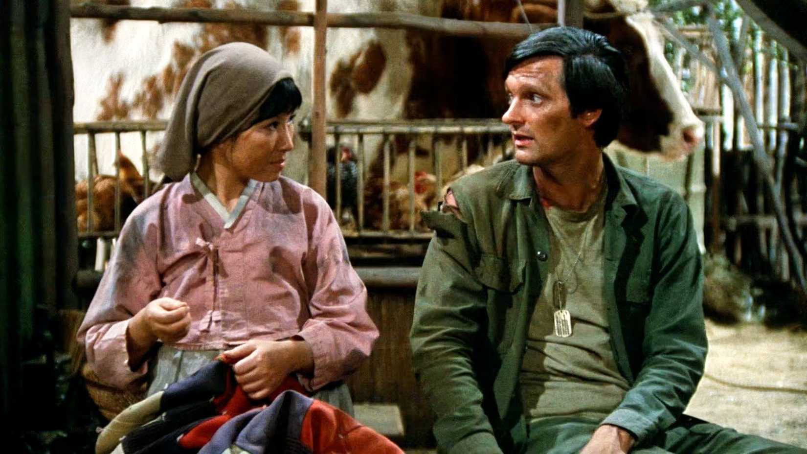 Hawkeye sentado com uma mulher coreana costurando em M*A*S*H