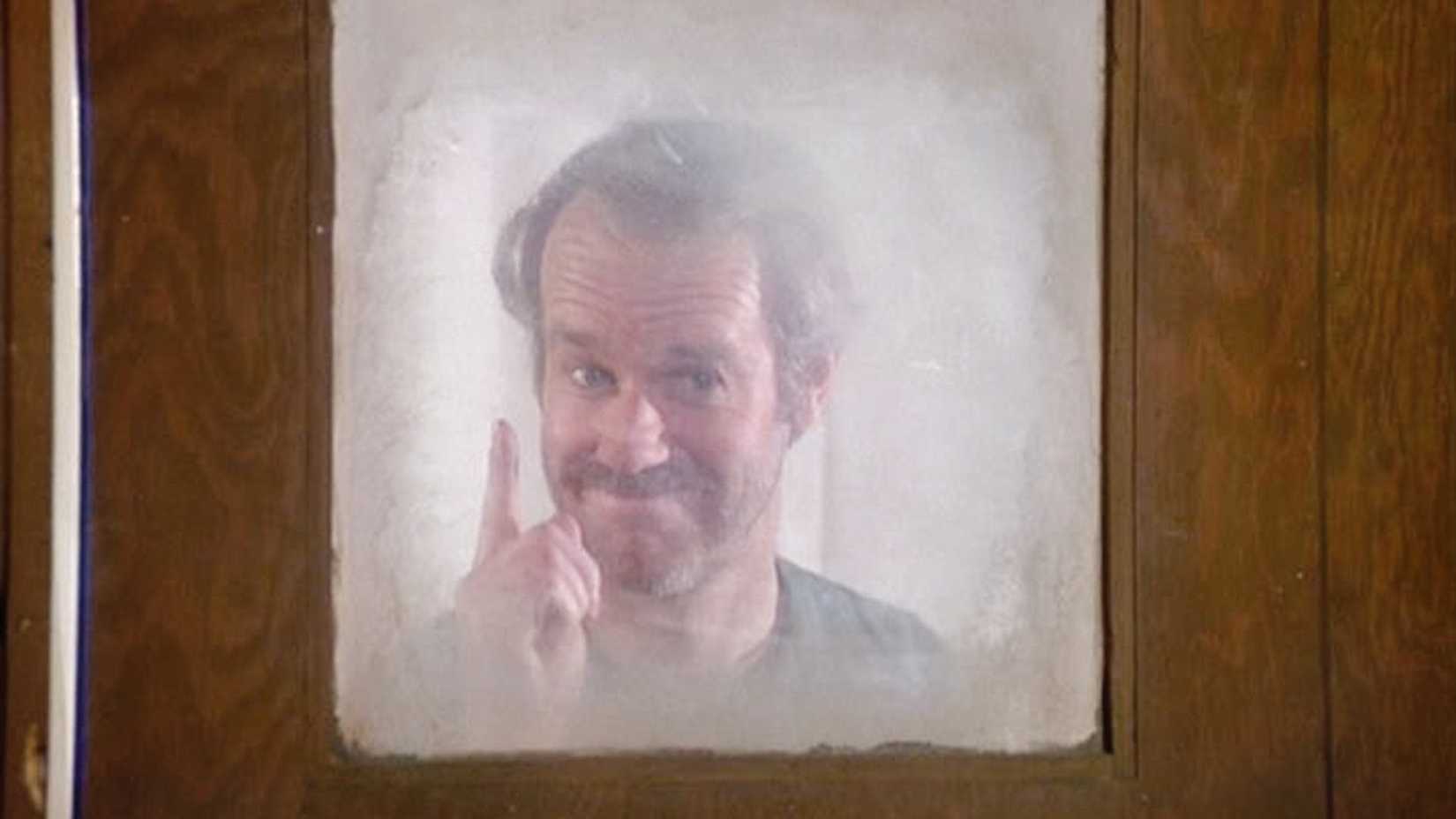 Mike Farrell como Hunnicutt sorrindo atrás de uma janela em M*A*S*H