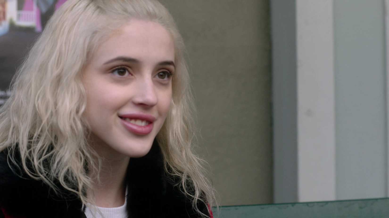 Max de Supernatural temporada 14 usando uma jaqueta com gola preta e sorrindo.