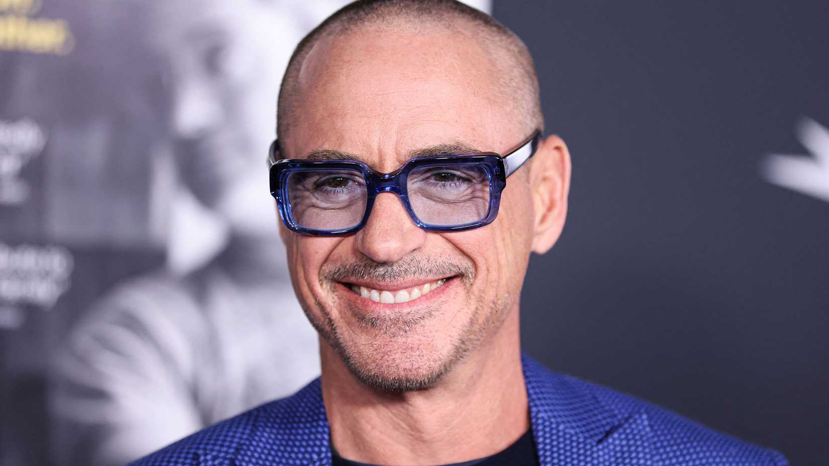 Shaven-headed Robert Downey Jr. wears chic blue glasses and smiles while attending an event