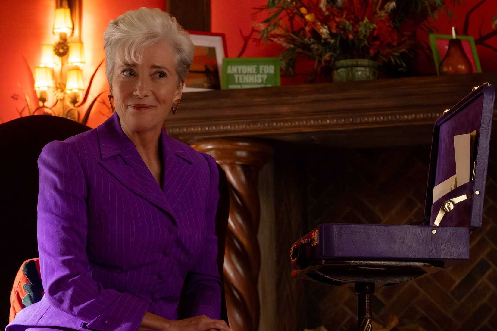 Emma Thompson sits in a living room wearing a purple suit and smiling at someone off-camera in The Sheep Detectives. 