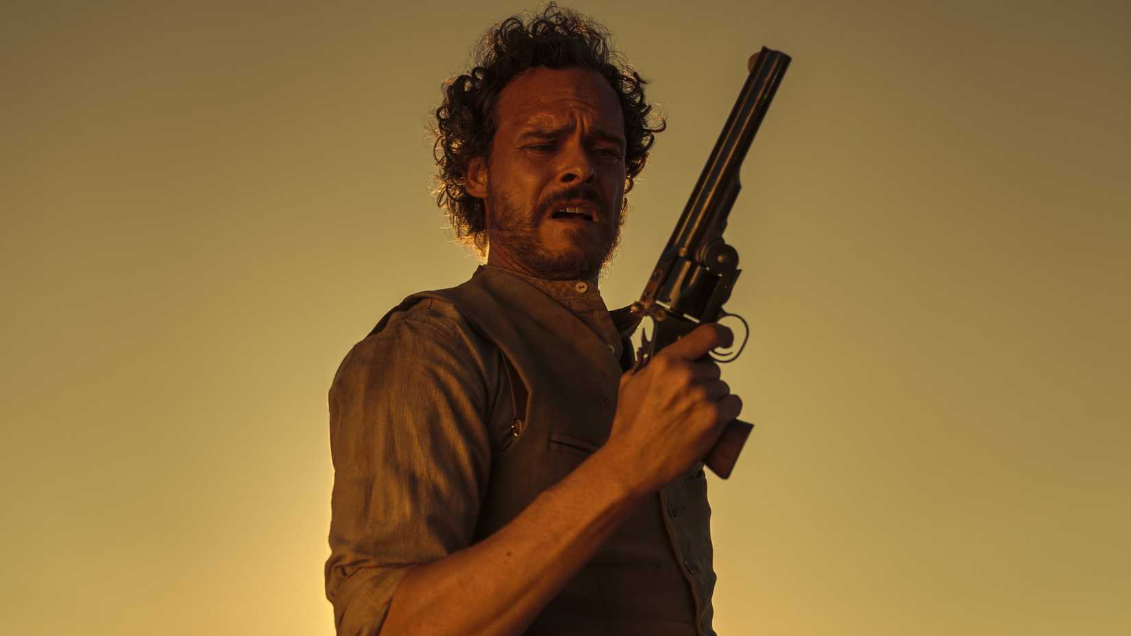 Miguel Alvarez as Timothy Flynn holding a pistol in The English (2022)