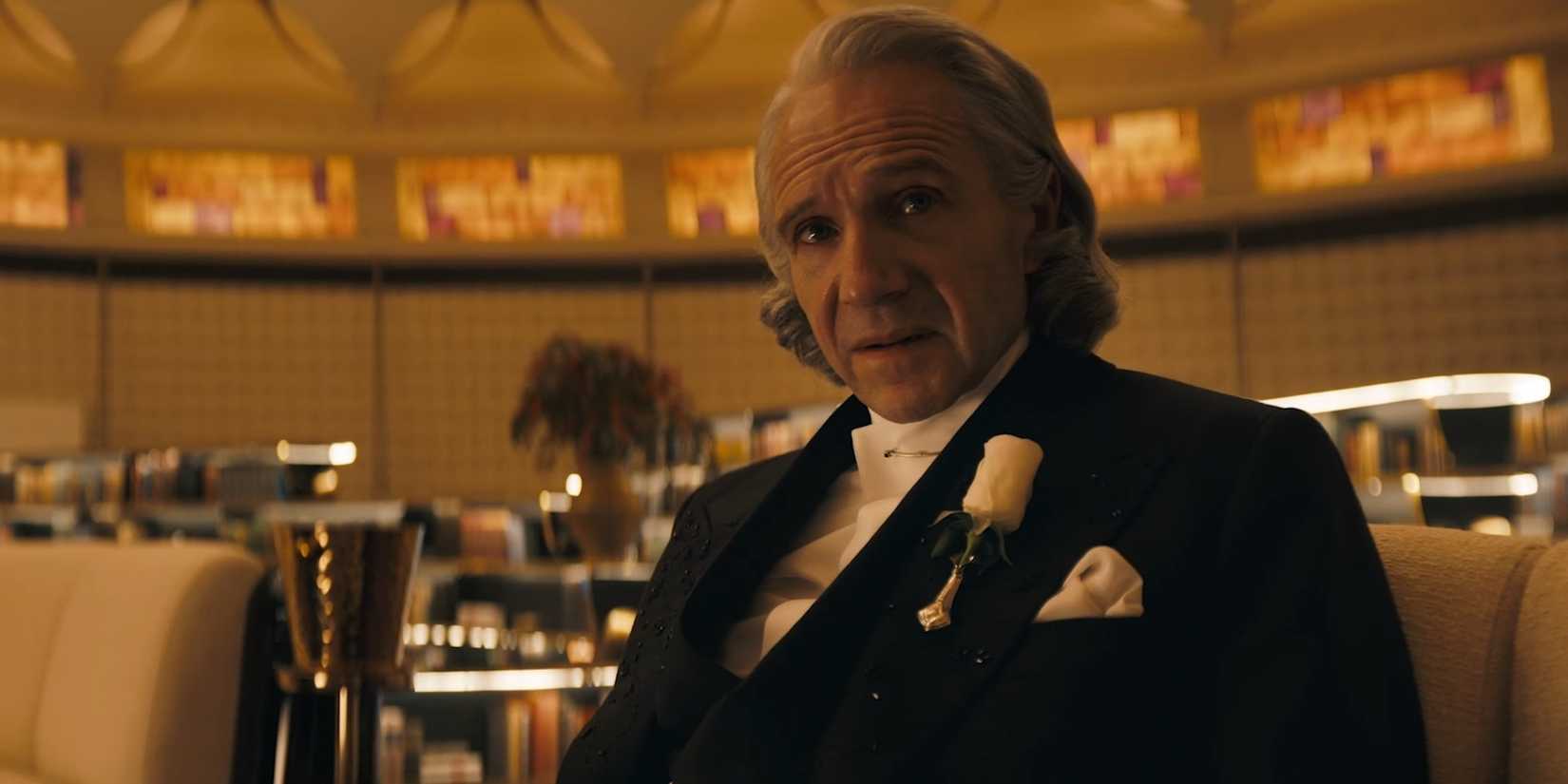 Ralph Fiennes como Presidente Snow em um terno vermelho em The Hunger Games: Sunrise on the Reaping.