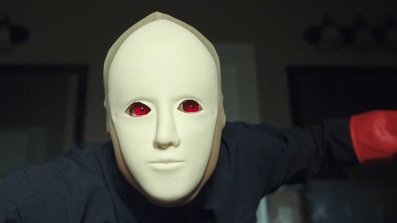 O assassino olhando para a câmera com máscara branca e lentes vermelhas em Faces of Death