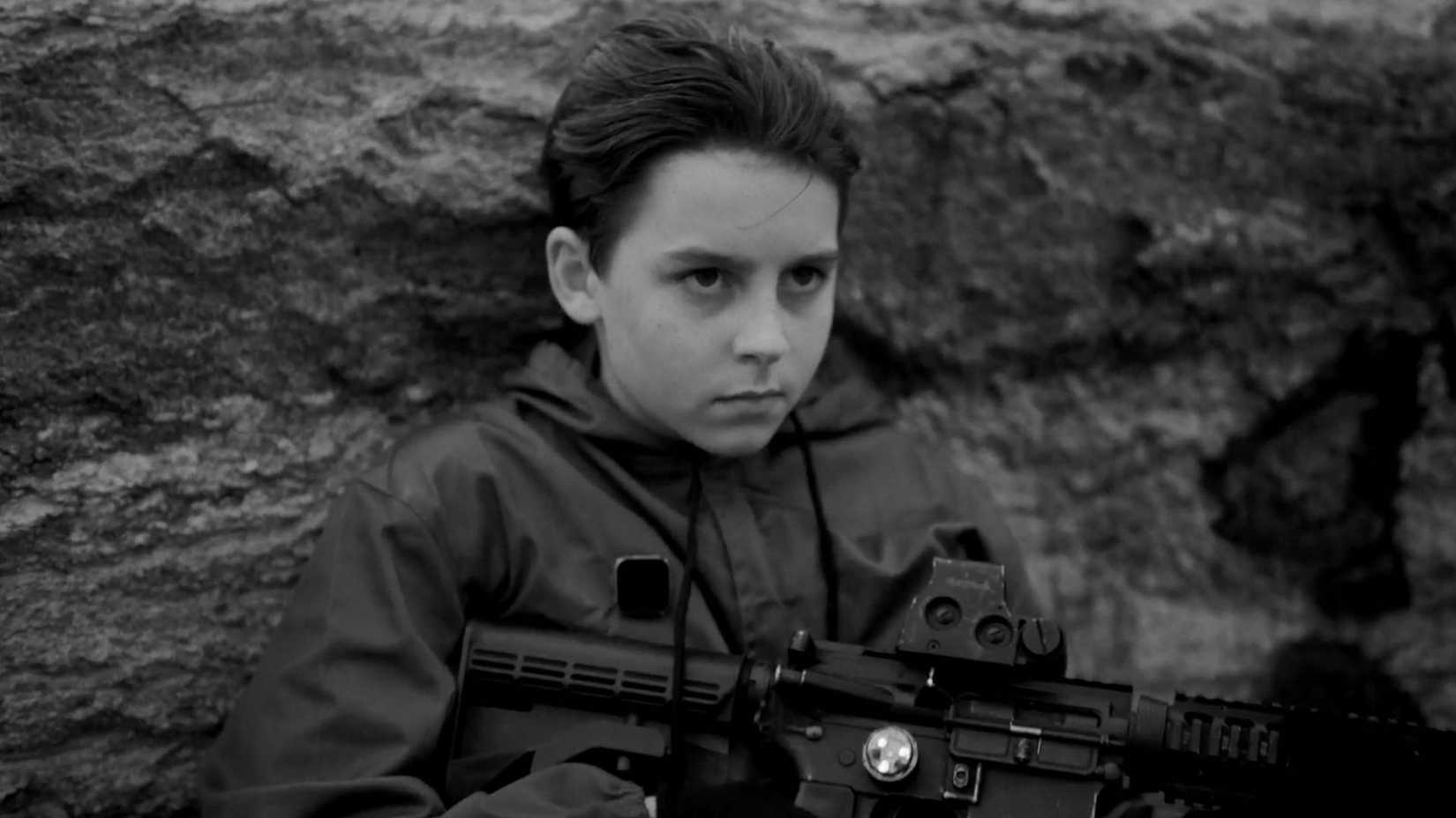 A child holds a gun and stares past the camera