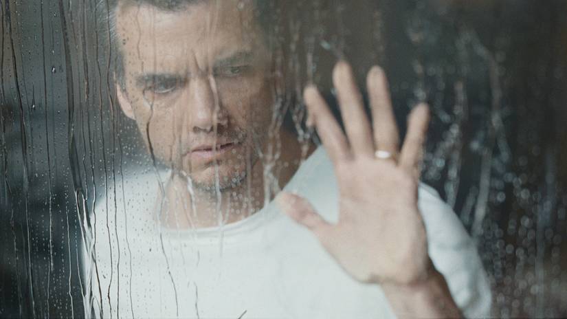 Wagner Moura touches a window while peering hopelessly in a scene from The Last House