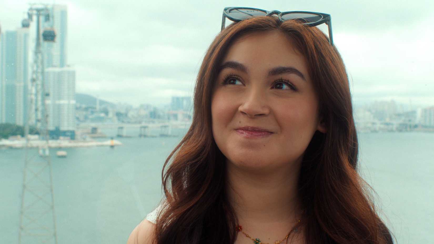 Kitty & Min Ho's Relationship Status 2 xo kitty season 3 still featuring kitty song covey wearing sunglasses on top of her head with the seoul skyline in the background.