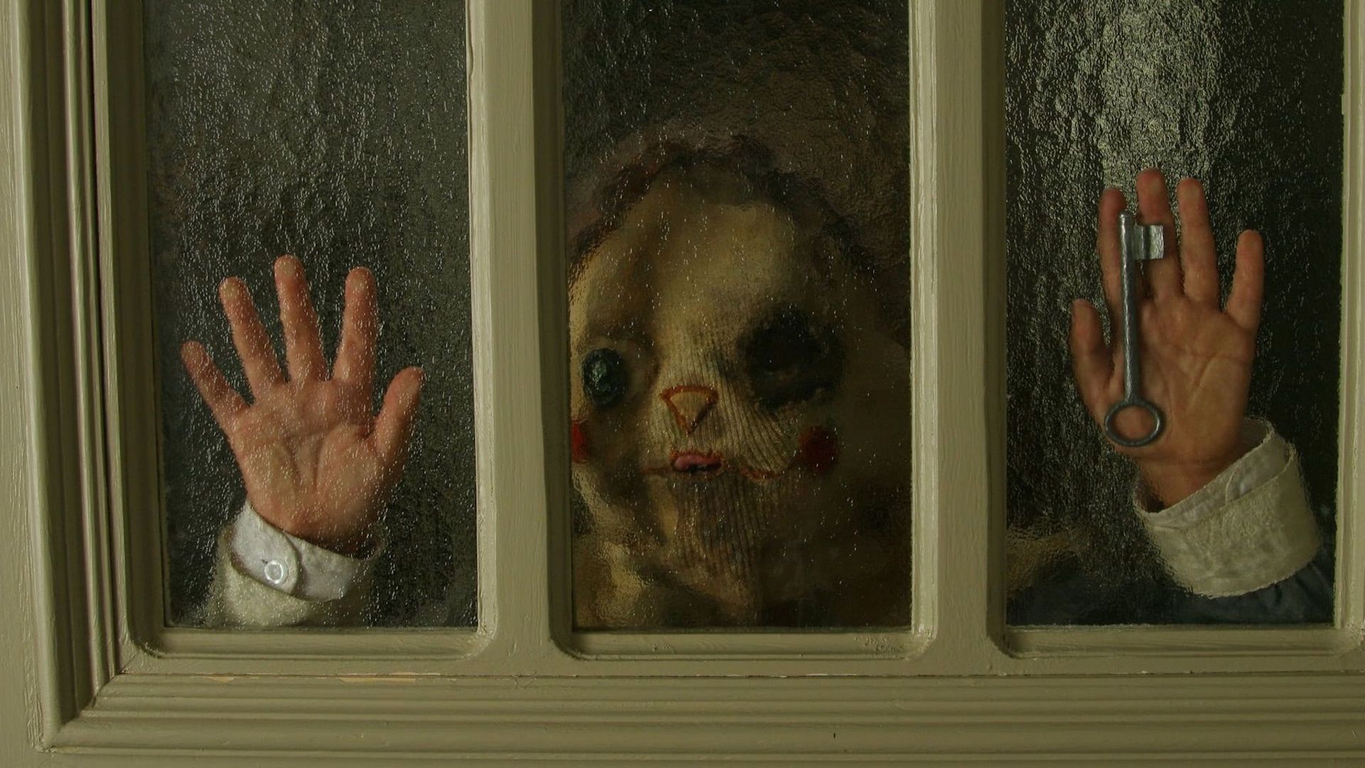 A child standing at a door window holding a key wearing a creepy mask in Orphanage-1