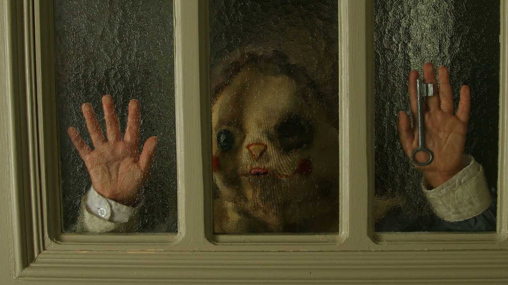 A child standing at a door window holding a key wearing a creepy mask in Orphanage