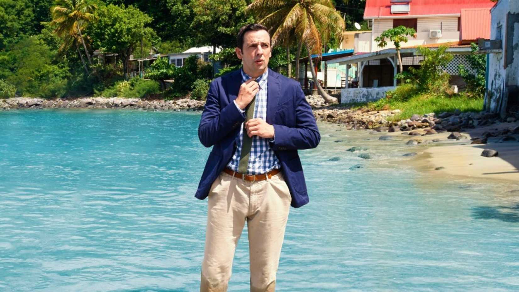 A person fixing their tie while in the water in Death in Paradise