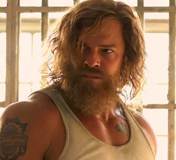 Alan Ritchson as John Miller standing in front of bars with a tense expression on his face in Motor City