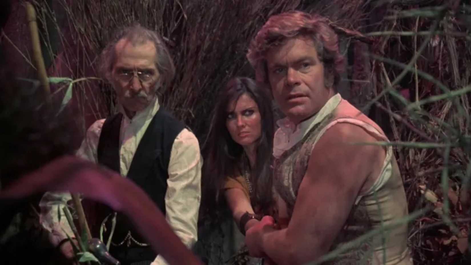 Three people walk through the woods in At Earth's Core